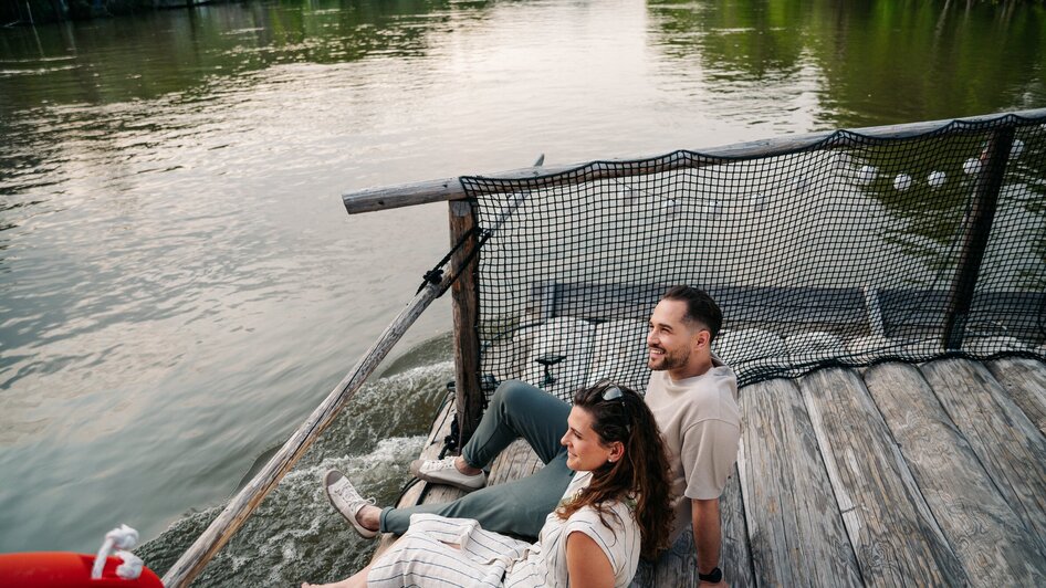 Paar sitzt am Fluss und genießt die Aussicht beim Floßfahren.