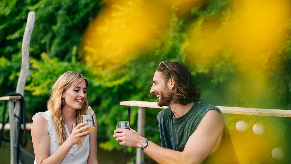 Ein Paar genießt Cocktails in entspannter Atmosphäre beim Floßfahren auf der Mur in Graz.