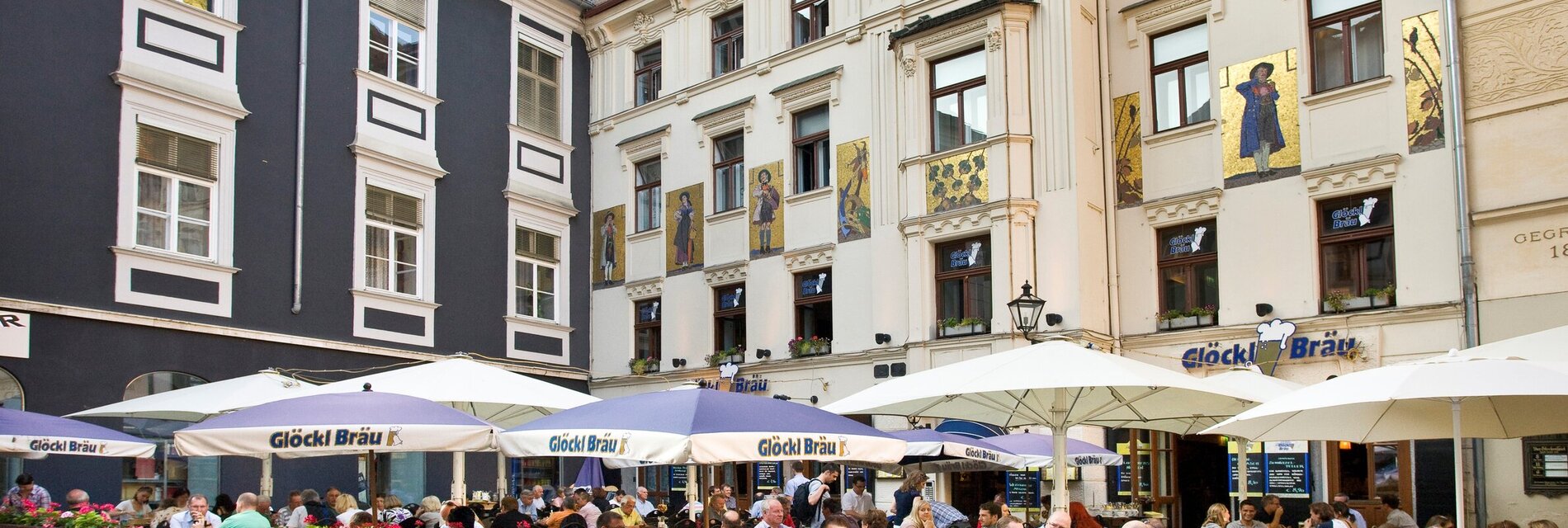 Außenansiht der Apartments am Glockenspielplatz mit Gäste im Gastgarten davor