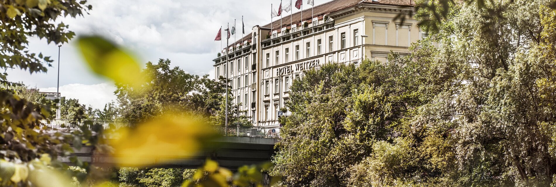 Außenansicht des Hotels Das Weitzer am Fluss Mur mit grüner Umgebung.