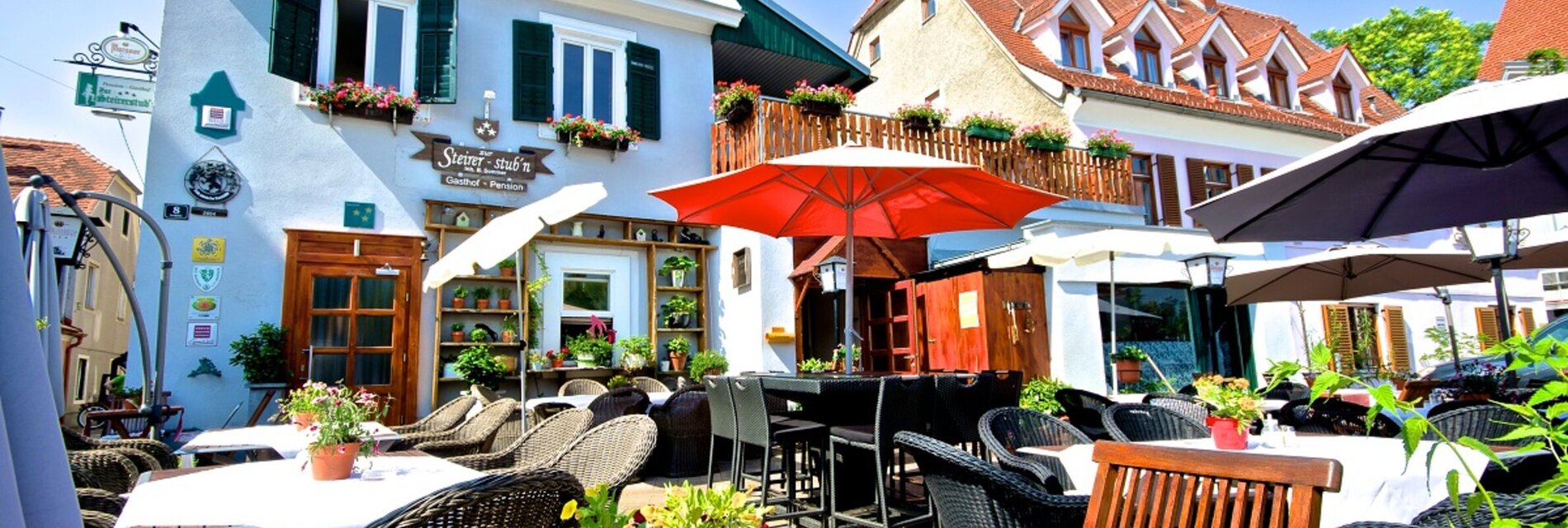 Terrasse des Gasthofs mit Pflanzen und Sonnenschirmen.