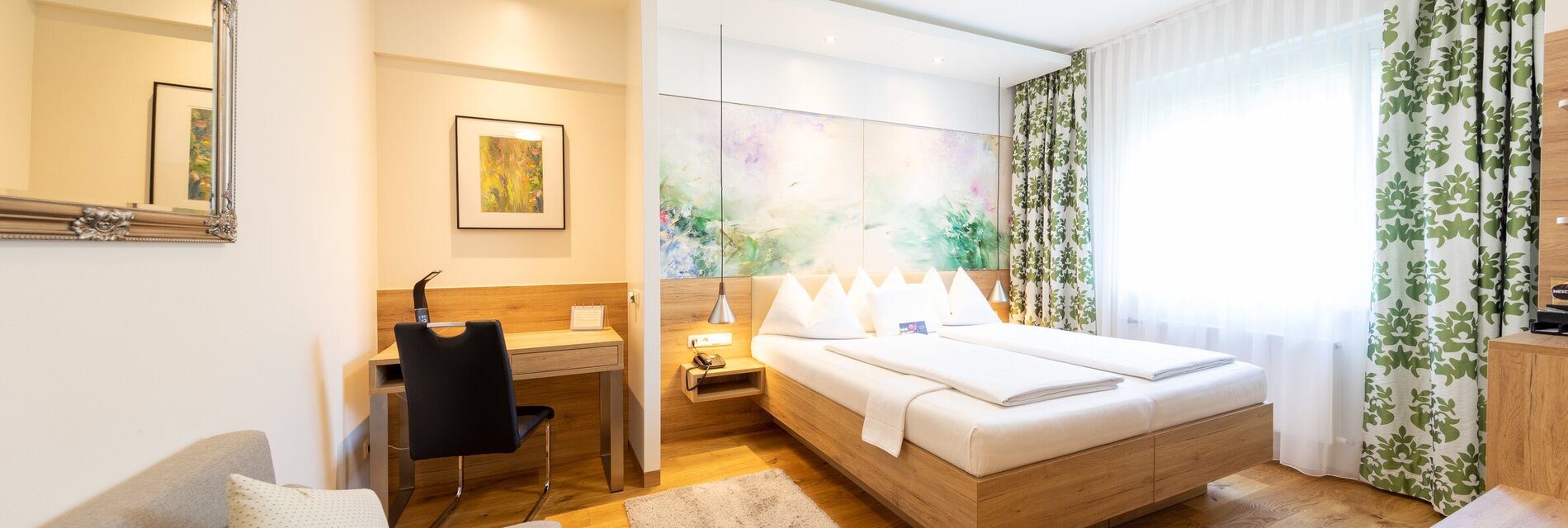 Helles Zimmer mit Doppelbett, Schreibtisch und Sofa.
