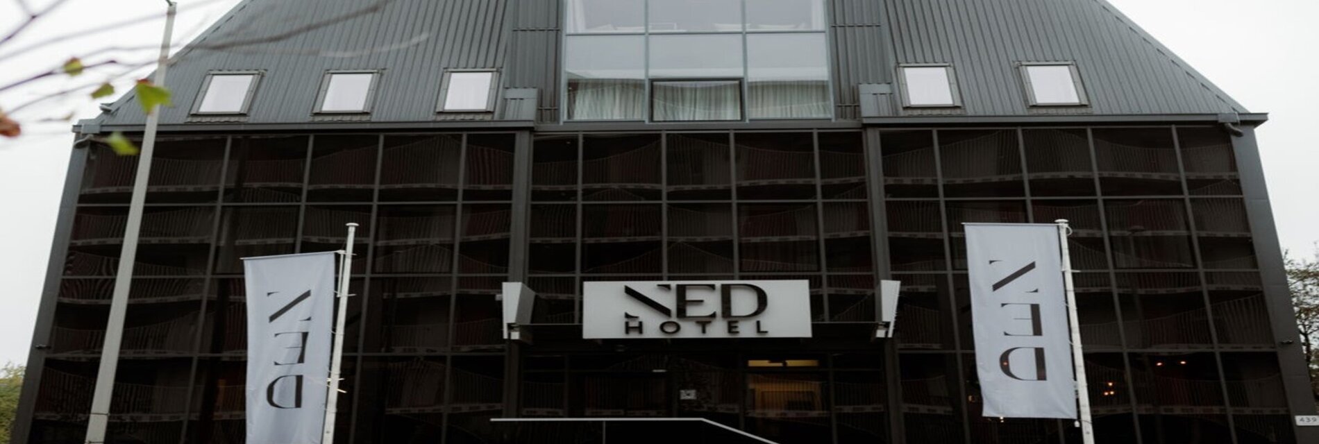 Das NED Hotel in Graz mit Spiegelglasfassade und Hotelbanner.