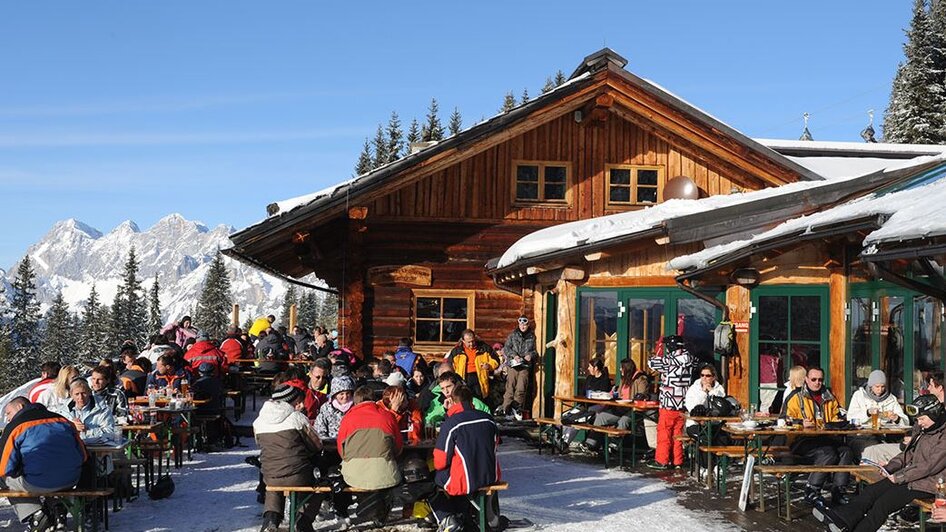 Holzhütte im Schnee mit Terrasse voll mit Menschen